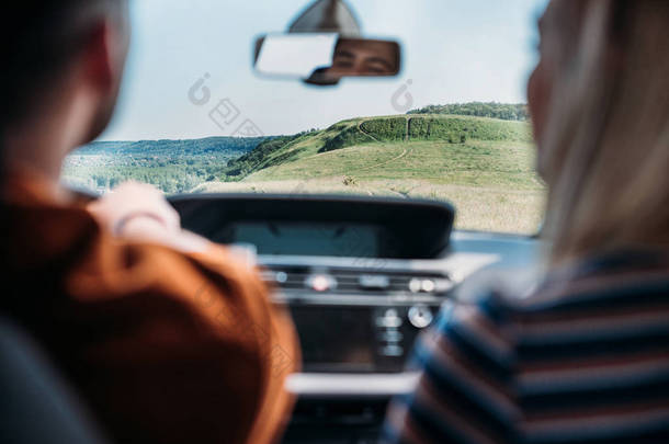 乡村草地上坐小汽车的年轻夫妇的后视 