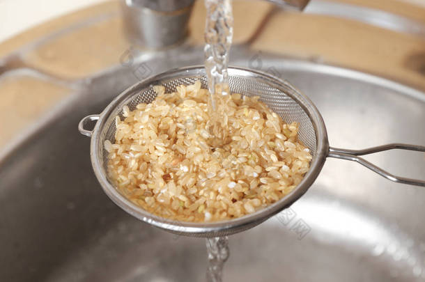 在厨房的水槽洗涤原料糙米在漏勺