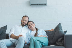 微笑的夫妇坐在沙发上夏季热在家中与空调在墙上