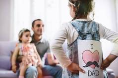 父亲节快乐的概念。儿童女儿隐藏惊喜明信片礼物给她的爸爸.