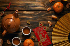 在木桌上可以看到带有象形文字、金色中国装饰、茶具和橘子的扇子的顶视图 