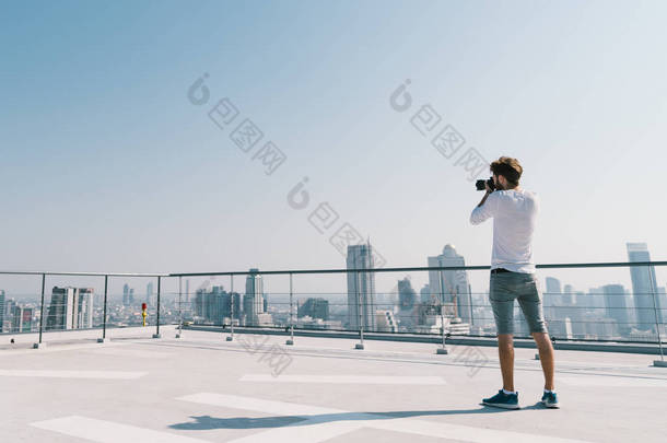 年轻白人白人男子在阳光明媚的一天, 在屋顶上拍摄城市景观照片。摄影嗜好、<strong>小工具</strong>技术或休闲活动概念。蓝天上的复制空间