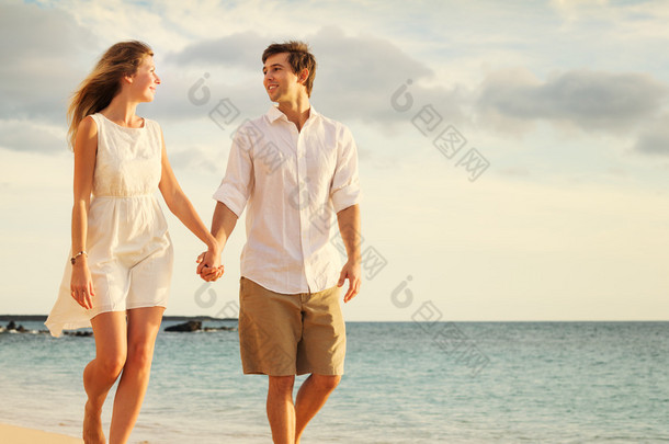 年轻的夫妇在海滩上散步，在夕阳的爱