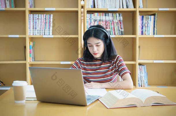 一个女大学生坐在桌旁做大学<strong>图书馆</strong>的作业。 学生使用笔记本电脑，在网上学习.