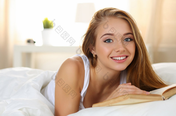 年轻美丽微笑的金发女人躺在床上看书