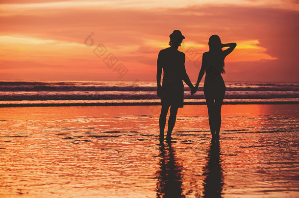 对年轻夫妇的剪影爱好不容易才开始在沙滩上美丽夕阳红为背景