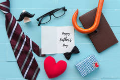 快乐的父亲日概念。红领带, 眼镜, 胡子, 笔记本, 礼品盒与快乐的父亲节文本和手工红色的心在明亮的蓝色粉彩木桌背景.