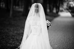 一个美丽的新娘独自走在公园的肖像。黑白照片.