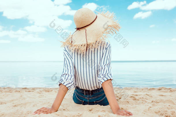 在沙滩上放松稻草帽的妇女后视图 