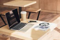 带空白屏幕的笔记本电脑、智能手机和商务报纸在咖啡店的餐桌上