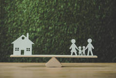 剪纸房子和纸家庭平衡在绿色背景的跷跷板