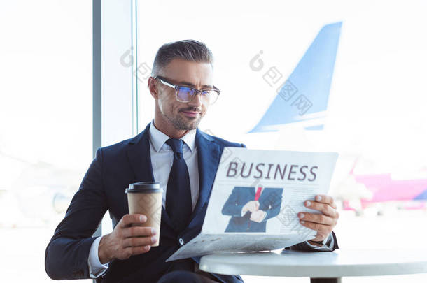 成人英俊的商人读报纸和拿着咖啡去机场