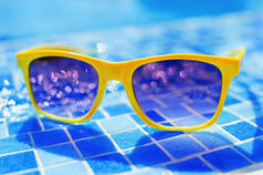 Yellow sunglasses on a background of a pool with water.