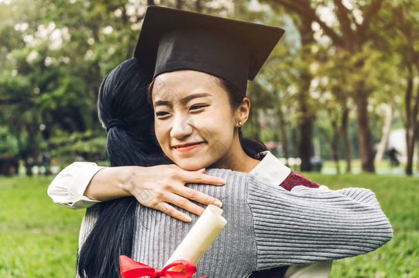 成功的学生年轻女子和学士礼服与文凭毕业生拥抱她的朋友在大学。庆祝毕业和教育理念