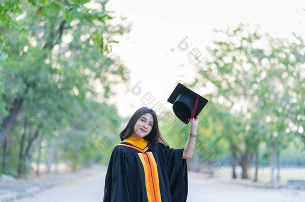 一位穿着学术礼服头戴研究生帽的年轻快乐的女毕业生在大学校园里开始庆祝她的大学学位.