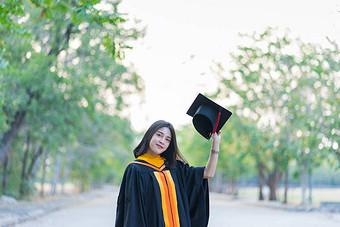 一位穿着学术礼服头戴研究生帽的年轻快乐的女毕业生在大学校园里开始庆祝她的大学学位.
