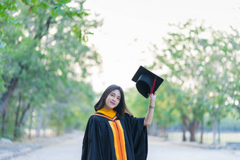 一位穿着学术礼服头戴研究生帽的年轻快乐的女毕业生在大学校园里开始庆祝她的大学学位.图片