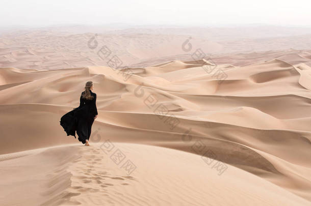 长袍的年轻女子在沙漠景观中摆姿势.