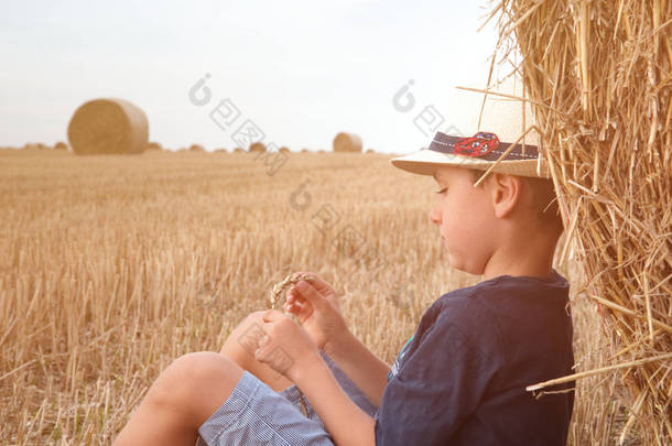 可爱的乡村男孩在附近草垛在日落时在夏天的帽子。夏天的概念，一个假期。与温暖的夏日儿童户外活动休闲.