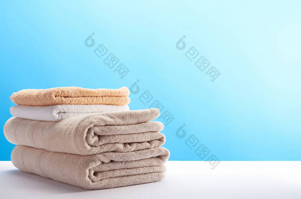 一叠干净的新鲜柔软的毛巾在蓝色的背景 
