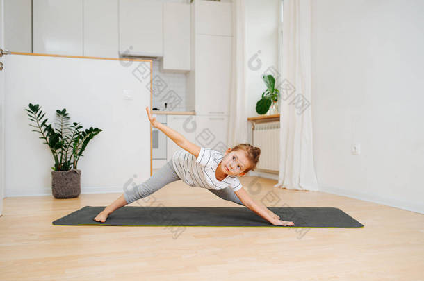 小女孩在家里的垫子上做瑜伽。她前倾，两条腿分开，一边伸直了<strong>胳膊</strong>，另一边伸直了<strong>胳膊</strong>.