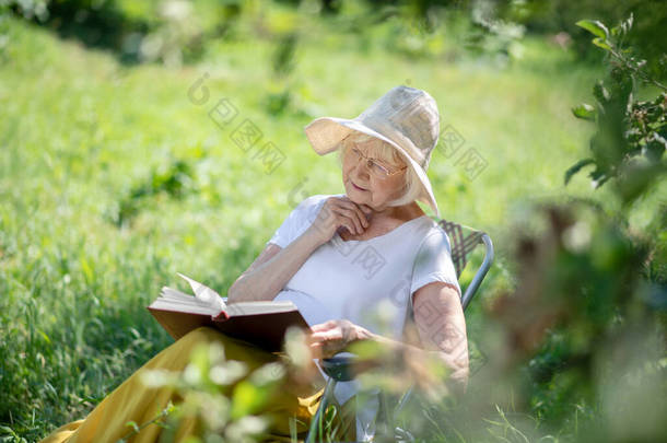 在户外看书的松懈的老年妇女