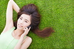 微笑的女孩躺在一片草地上，用智能手机通话
