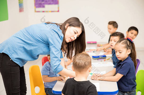 可爱的女学龄前教师耐心地解释他的工作分配她的一个学生在<strong>教室</strong>里