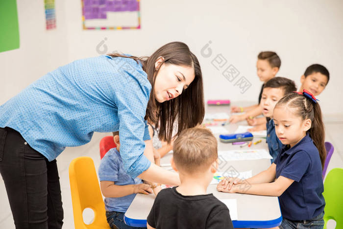 可爱的女学龄前教师耐心地解释他的工作分配她的一个学生在教室里