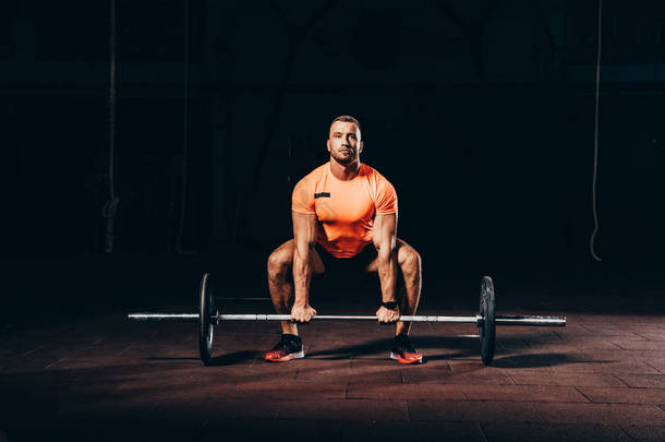 英俊的运动健美运动员在黑暗的健身房<strong>举重杠铃</strong>