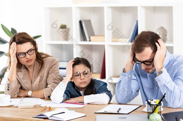 可爱的孩子在眼镜坐在疲惫的父母在办公室 