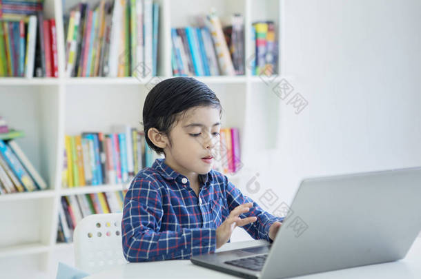在图书馆里使用笔记本电脑的小男孩