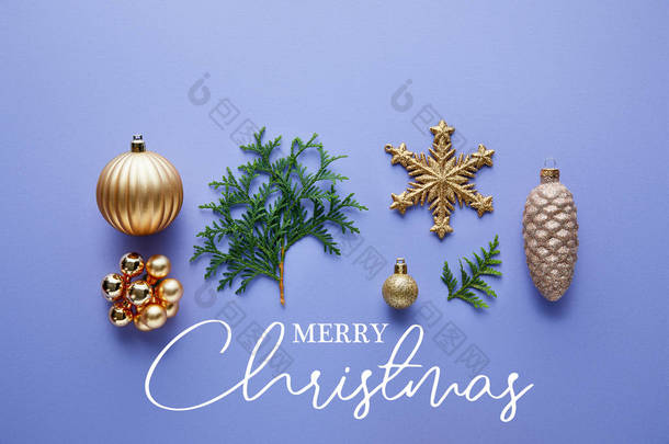 明亮的金色圣诞装饰的顶部视图，蓝色背景的绿色thuja枝条，附有圣诞快乐的插图