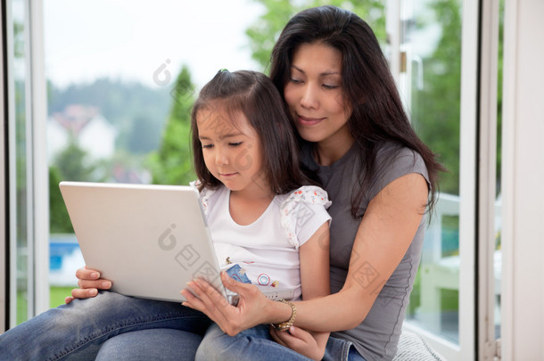 可爱的女儿和母亲与便携式计算机