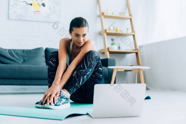 家庭妇女坐在笔记本电脑旁的健身垫上的有选择的焦点 