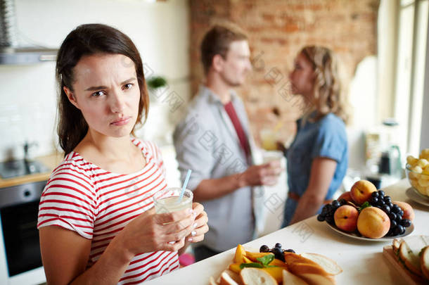 嫉妒的<strong>女孩</strong>与自制的饮料看着相机在年轻夫妇的背景下交谈