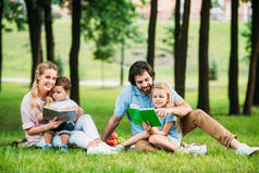 美丽的年轻家庭坐在草地上的公园和阅读书籍