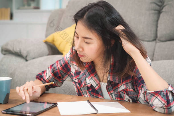 亚洲女学生在家做作业，女学生喝咖啡，在客厅里用平板电脑搜索沙发。生活方式的女人在家里放松一下.