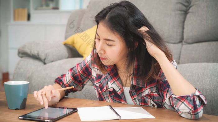 亚洲女学生在家做作业，女学生喝咖啡，在客厅里用平板电脑搜索沙发。生活方式的女人在家里放松一下.