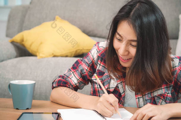 亚洲女学生在家里<strong>做作业</strong>，女学生在客厅用平板电脑搜索沙发。生活方式的女人在家里放松一下.