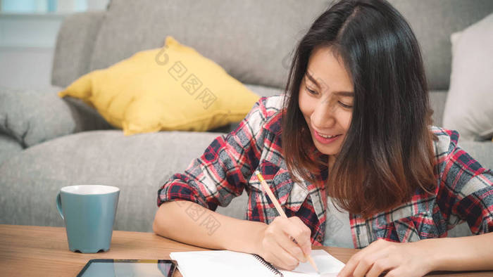 亚洲女学生在家里做作业，女学生在客厅用平板电脑搜索沙发。生活方式的女人在家里放松一下.