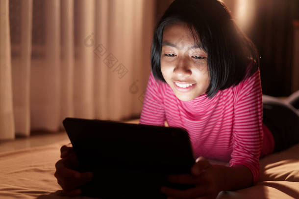  快乐的亚洲女孩在网上通过平板电脑<strong>学习</strong>，晚上在卧室里，亚洲孩子在电脑上<strong>看</strong>教育距离，脸上挂着笑容。在家<strong>学习</strong>概念