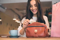微笑的妇女掏出现金从袋子在桌与咖啡杯子在咖啡馆里 