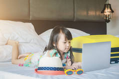 小女孩躺在笔记本电脑在床上快乐微笑使用互联网观看和乐趣在孩子的关系与技术概念