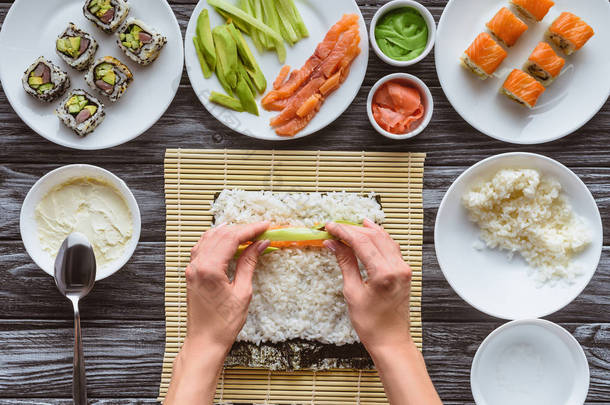 裁切拍摄的人烹饪美味的寿司卷与鲑鱼, 鳄梨和黄瓜
