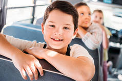 特写肖像微笑的小男孩骑在校车与模糊的同学在后台