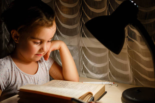 漂亮的小女孩看书坐在桌下灯儿童和教育