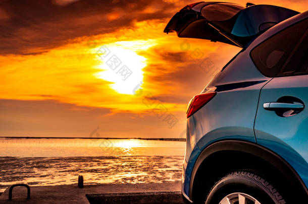蓝色紧凑型 Suv 车与体育和现代设计停放在具体道路上的海上日落。环境友好的技术。旅途旅行在海滩和打开汽车卡车的假日. 