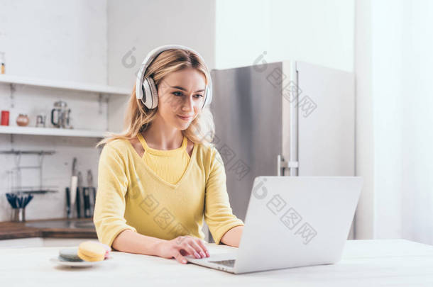 有吸引力的金发碧眼的女人听音乐在耳机, 而使用笔记本电脑