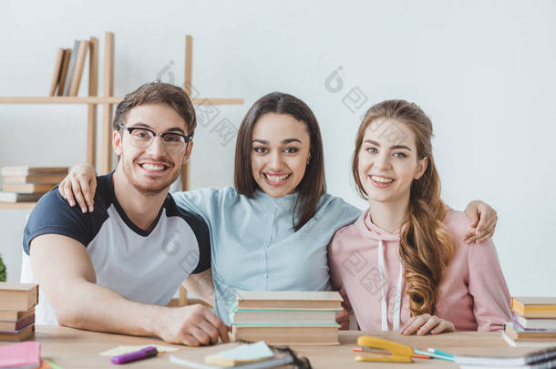 年轻的微笑的学生坐在桌与书  